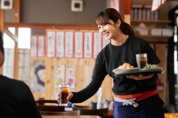 Smiling Japanese waitress dropping off drink at table in izakaya